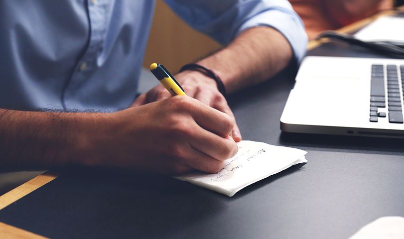 a man with formal shirt writing on paper on his deshk