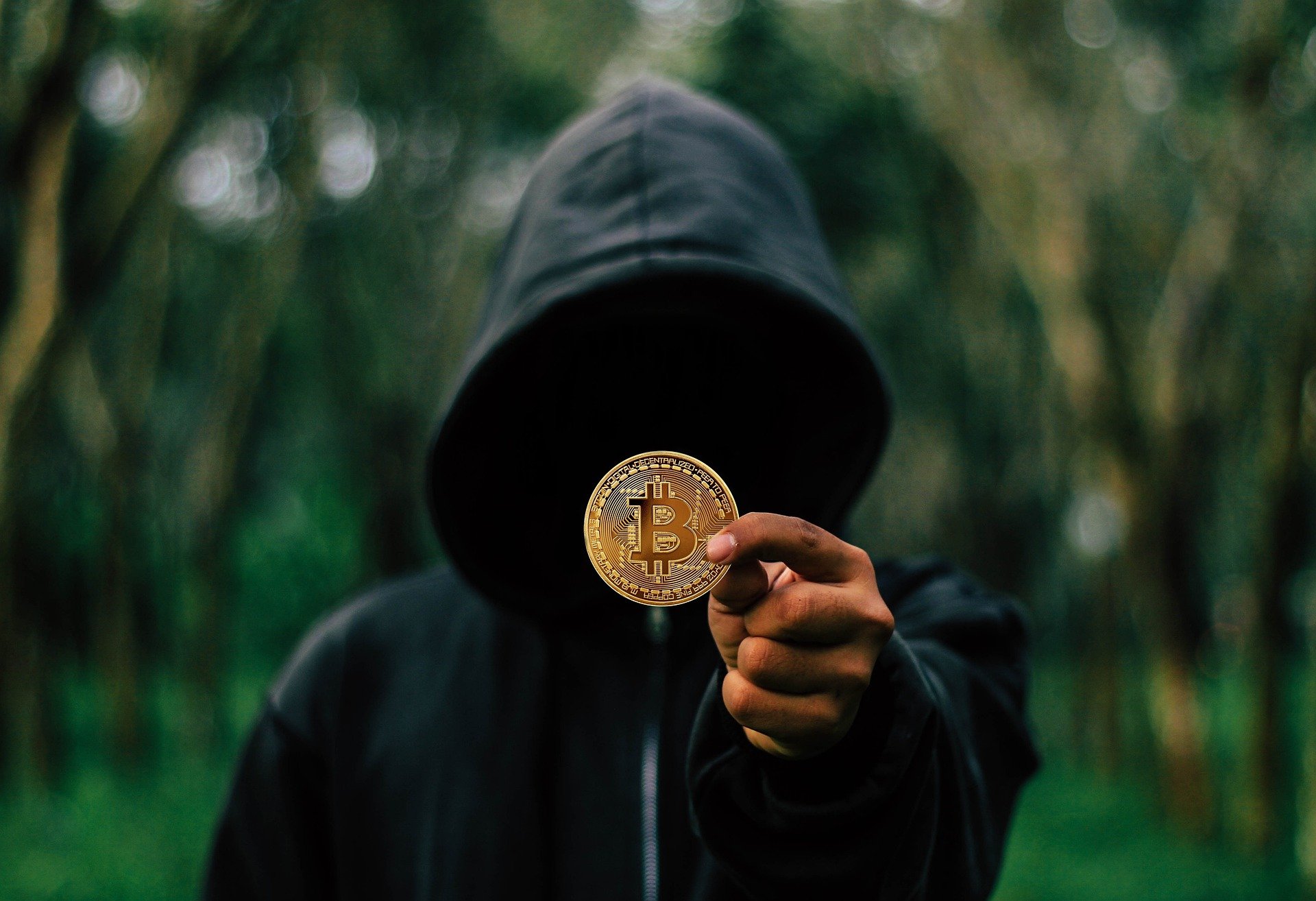 a black hoodie person or hacker showing bitcoin